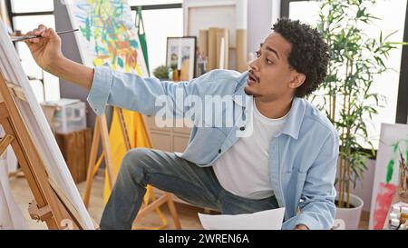 Focused young man painting on canvas in a bright, creative art studio setting, embodying inspiration and artistic endeavor. Stock Photo