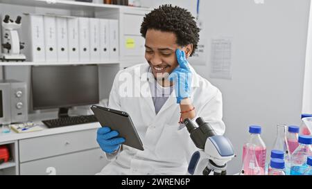 A smiling young man in lab coat using tablet in modern laboratory setting. Stock Photo
