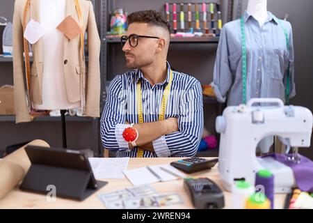 Hispanic man with beard dressmaker designer working at atelier looking to the side with arms crossed convinced and confident Stock Photo