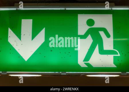 Illuminated green exit sign with integrated lights. Dead insects and rests of spider webs on the surface. Stock Photo