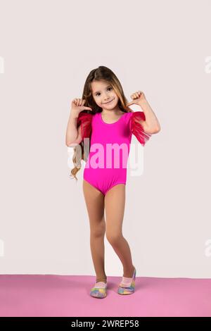 Full length vertical shot of a little blonde girl in a gymnastic outfit pointing fingers at her isolated on a white background. High quality photo Stock Photo