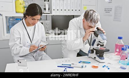 Man and woman scientists in laboratory, working with microscope and taking notes for research. Stock Photo