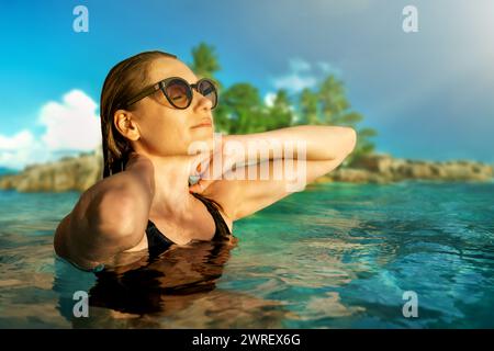 woman with sunglasses enjoying vacations and sunlight on face in ocean at tropical Seychelles islands Stock Photo