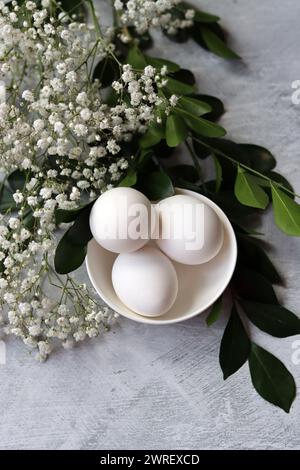 Simple composition still life with eggs and white flowers. Easter celebration concept. Eggs in a white ceramic bowl top view photo. Stock Photo