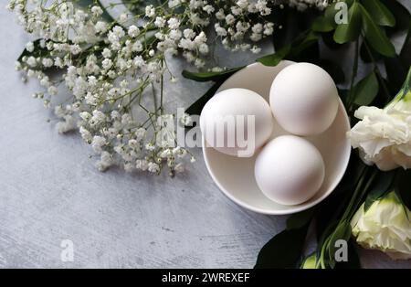 Simple composition still life with eggs and white flowers. Easter celebration concept. Eggs in a white ceramic bowl top view photo. Stock Photo