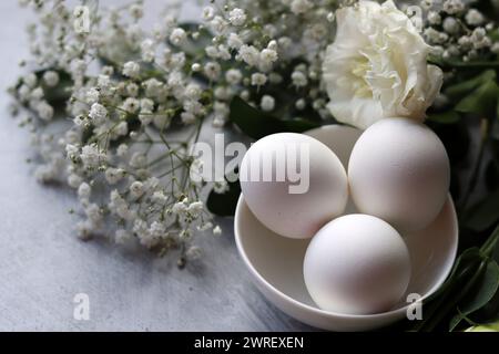 Simple composition still life with eggs and white flowers. Easter celebration concept. Eggs in a white ceramic bowl top view photo. Stock Photo