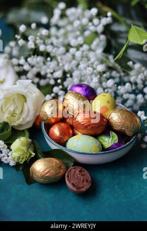 Foil wrapped Easter chocolate eggs in a glass bowl. Easter celebration concept. Colorful still life with sweets. Textured background with copy space. Stock Photo