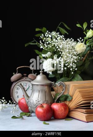 Still life photo of vintage metal teapot, old book and red apples on a table. Retro aesthetic concept. Stock Photo