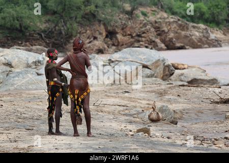 Two Ethiopian girls from a tribu Hamer are situated on the bank of the river Omo and look towards the river. Stock Photo