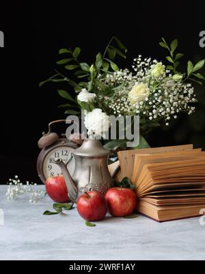 Still life photo of vintage metal teapot, old book and red apples on a table. Retro aesthetic concept. Stock Photo