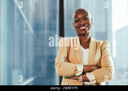 Confident black businesswoman in the office stands with her arms crossed, portraying success and professionalism. She exudes confidence and happiness Stock Photo