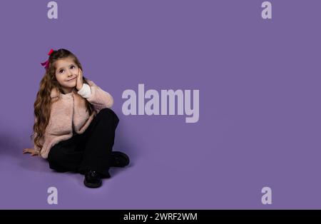 The picture on a purple background with a small and stylish girl dressed in a surprised way as she sits engrossed and thinks about some coins that mak Stock Photo