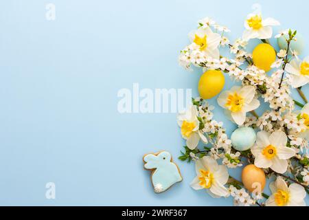 Festive background with spring flowers and naturally colored eggs and Easter bunnies, white daffodils and cherry blossom branches on a blue pastel bac Stock Photo