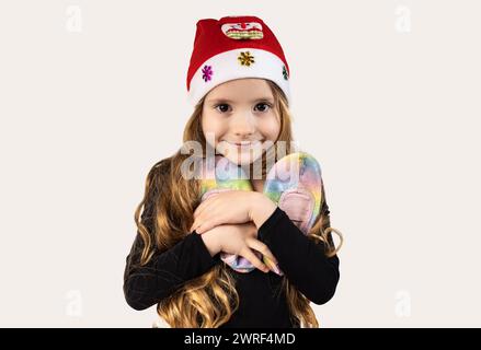 The portrait of a tender, gymnast girl dressed in a black jumpsuit and with a Santa hat on her head hugs her ballerinas. Concept of love of Sport and Stock Photo