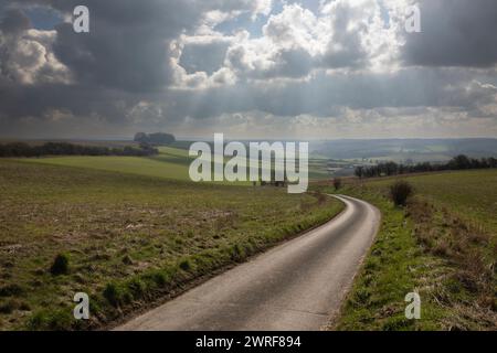 Empty single track country lane running down through open farmland with dramatic sky above, School Lane, East Garston, Berkshire, England, UK Stock Photo