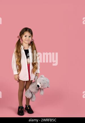 A little blonde girl with two pigtails holding her gray teddy bear, full length portrait, Valentine's day concept. High quality photo Stock Photo