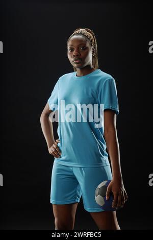 Vertical portrait of African American woman as female soccer player posing with confidence against black background and holding ball Stock Photo
