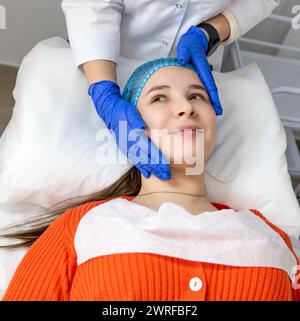 Cosmetologist putting hands on client's face, preparing for beauty procedures. Calm model lying on cosmetic chair with eyes open, waiting for facial m Stock Photo