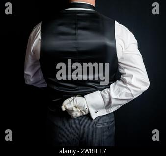 Portrait of Back of Butler or Hotel Concierge in Black Vest or Waistcoat Holding Hand Behind Back in Attitude of Graceful Civility. Service Industry a Stock Photo