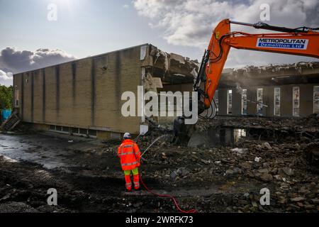 Demolition site (man in hi-vis working hosing rubble, building deconstruction, controlled collapse, empty shell) - Baildon, West Yorkshire England UK. Stock Photo