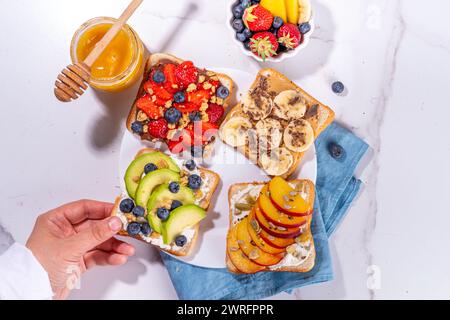 Fruit berry sandwiches. Various toasts with peanut butter, cream cheese, chocolate spread with summer berries and fruits - strawberry, banana, peach, Stock Photo