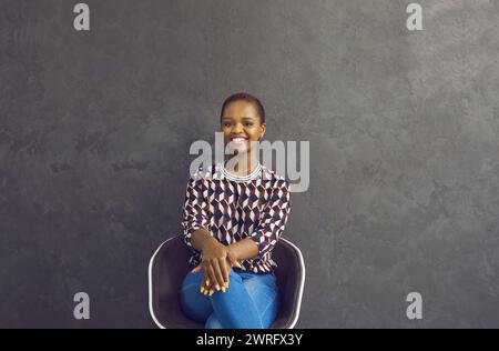 Portrait of happy millennial African American woman sit on chair Stock Photo