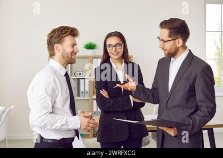 Three business people standing in office at the workplace discussing successful deal. Stock Photo