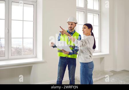 Meeting female homeowner and builder in living room for further renovation work.Attentive foreman in helmet and overalls with document or technical Stock Photo