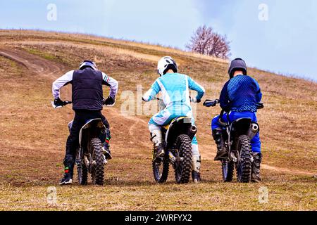 Three motorcyclists are riding their bikes on a dirt road through a grassy terrain under the clear sky, wearing helmets for safety Stock Photo
