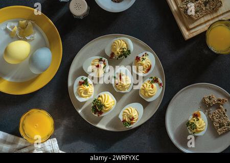 Deviled eggs, orange juice, healthy crackers, dyed eggs on dark gray background with sunligh and harsh shadows, directly above, high angle view. Happy Stock Photo