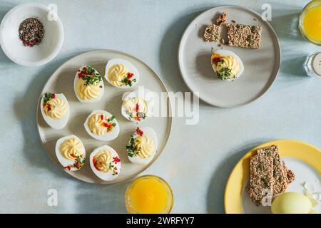 Deviled eggs, orange juice, healthy crackers, dyed eggs on light blue background with sunligh and harsh shadows, directly above, high angle view. Happ Stock Photo