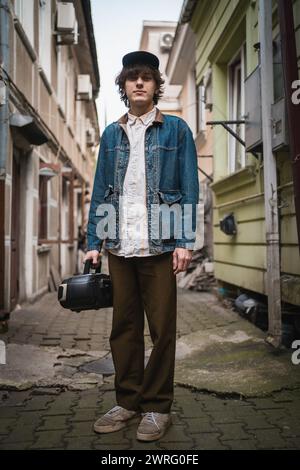 Stylish young man with vintage cassette player in old city alley. Modern retro fashion in hip culture. Vertical image Stock Photo
