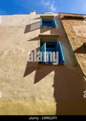 Traditional blue window, open wooden shutter, small white curtain on pink wall background. Under view of building facade, blue sky. Vertical Stock Photo