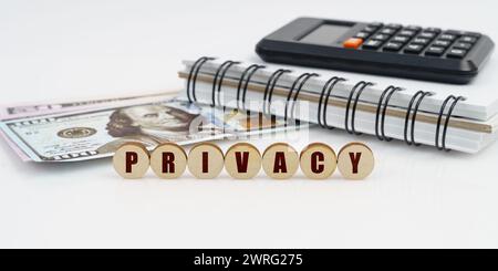 Business and finance concept. On a high surface lie a notepad, a calculator, dollars and wooden circles with the inscription - PRIVACY Stock Photo