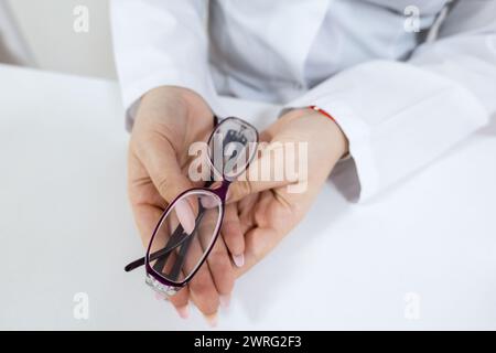 A woman is holding a pair of glasses in her hands, showcasing the latest fashion accessory in vision care. Her thumb is resting on the frame, creating Stock Photo