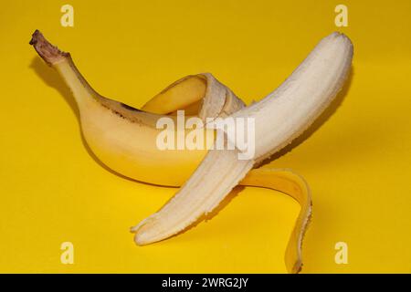 The picture on a yellow background shows a peeled yellow banana. Bananas are the best fruits, they are loved by children. High quality photo Stock Photo