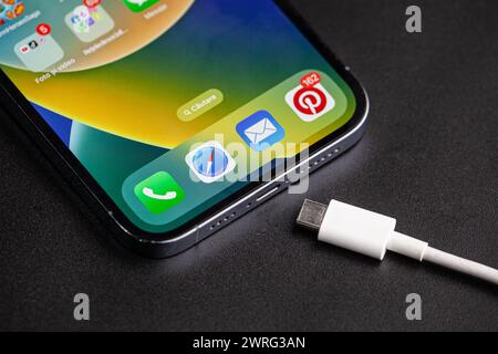 The picture of the iPhone with the type c charger next to it, which is the change of the year in telephone technology, on a black background.Hincesti Stock Photo