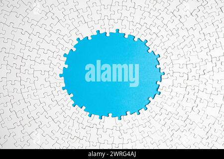 Plain white jigsaw puzzle  on blue  color background, oval shaped frame, abstract backdrop Stock Photo