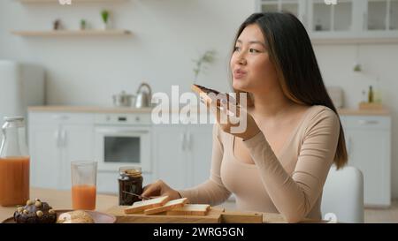 Asian korean woman eat sweet sandwich at home chinese girl female housewife cooking breakfast with bread and chocolate paste order food from Stock Photo