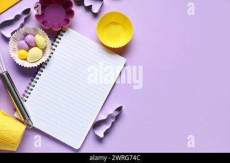 Blank notepad for recipes with Easter eggs and baking tools on lilac background Stock Photo