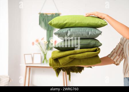 Woman holding stack of pillows with folded warm plaid in room Stock Photo