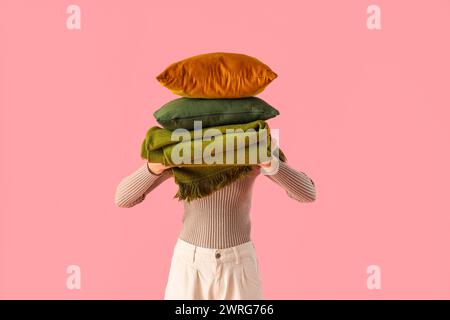Woman with stack of pillows and folded warm plaid on pink background Stock Photo