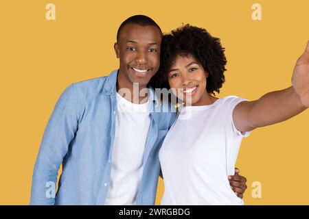 A joyful young couple taking a selfie, with the woman holding the camera and the man embracing her from behind Stock Photo