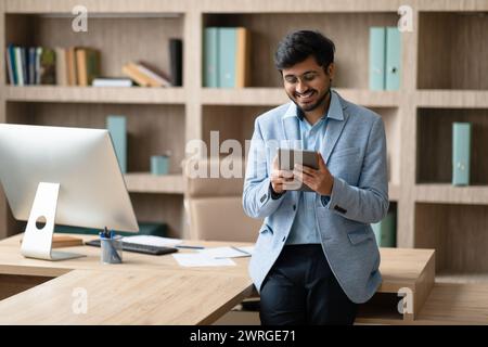 Cheerful Indian professional businessman websurfing on digital tablet in office Stock Photo