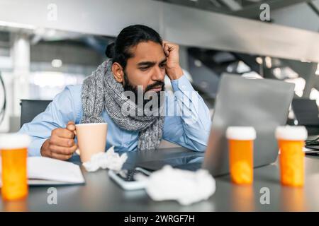 Exhausted sick indian guy employee working on laptop Stock Photo