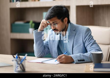 Indian entrepreneur man taking notes with concerned expression in office Stock Photo