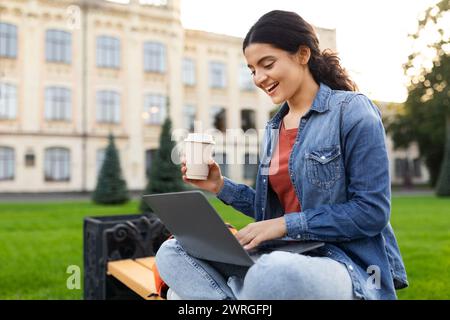 Pretty young indian woman sitting on bench, studying, using laptop Stock Photo