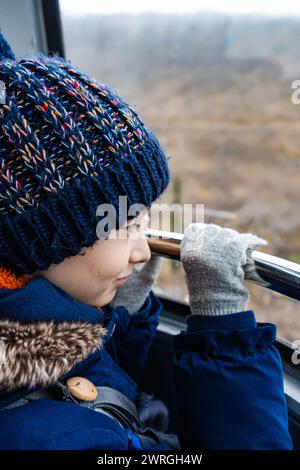Close-up of a boy wearing gloves looking out of the window and holding railings in a cable car, Georgia Stock Photo