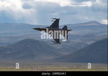 An F-16C Fighting Falcon assigned to the 706th Aggressor Squadron, conducts a familiarization flight over a low-level training area for Red Flag-Nellis 24-2, March 7, 2024. Red Flag provides participants the opportunity to plan and employ together in the air, domain (supported by space, and cyber) in a contested, degraded and operationally limited environment. (U.S. Air Force photo by William R. Lewis) Stock Photo