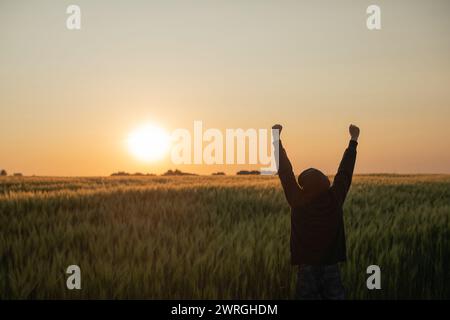 Rear view silhouette of a man standing in a field at sunset with his arms raised in the air, Belarus Stock Photo